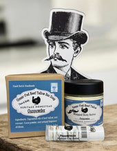 Load image into Gallery viewer, Heritage Homestead Gunpowder products including soap, body butter, and lip balm on a wooden surface.