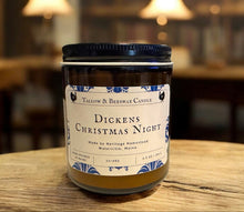Load image into Gallery viewer, dickens Christmas night tallow and bees wax candle on a wooden surface with a blurred library background with old books on shelves and lights.