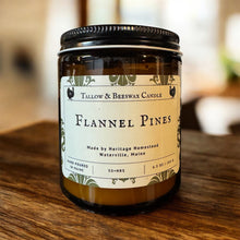 Load image into Gallery viewer, Candle jar labeled 'Flannel Pines' on a wooden surface with a blurred background