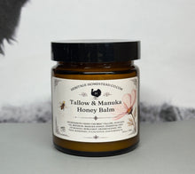 Load image into Gallery viewer, A jar of Heritage Homestead Co. Tallow & Manuka Honey Balm with a black lid and a cream-colored label, set against a soft gray background.