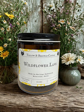 Load image into Gallery viewer, Tallow and beeswax candle labeled 'Wildflower Lane' with flowers in the background