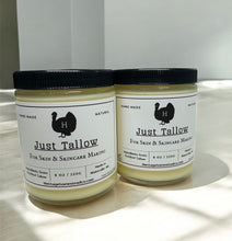 Load image into Gallery viewer, Two glass jars labeled "Just Tallow" sit on a light-colored surface in natural lighting. The jars are filled with a creamy, off-white substance and have black screw-top lids. The labels read "Hand Made," "Natural," and "Just Tallow – For Skin & Skincare Making." They indicate the product is made from grass-fed beef tallow and produced in Waterville, ME by Heritage Homestead Co. A black silhouette of a bird with an "H" on it is featured on the label.