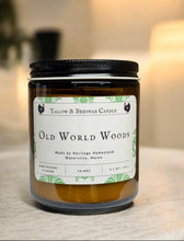 Load image into Gallery viewer, Candle jar labeled &#39;Old World Woods&#39; on a blurred background with another candle.
