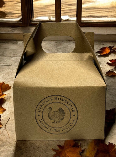 Small brown box with heritage homestead logo on it sitting on a porch with dried fall leaves around it. Includes our 5 tallow lip balms.