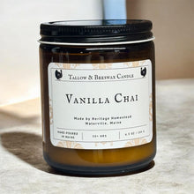 Load image into Gallery viewer, A Tallow &amp; Beeswax Candle in a dark amber glass jar with a black lid and a white label reading 'Vanilla Chai' on a neutral beige surface.
