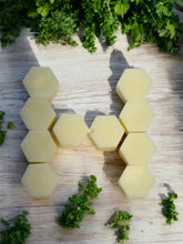Load image into Gallery viewer, Hexagonal tallow wax melts on a wooden surface with green herbs.
