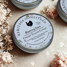 Load image into Gallery viewer, Blooming Grace creamy tallow lotion in a round metal tin by Heritage Homestead, a limited edition Mother’s Day floral scent handmade in Maine. Natural skincare product featuring grass-fed tallow, apricot oil, and clean ingredients for dry, sensitive skin. Rustic botanical styling with soft pink flowers, ideal gift for mom, nourishing tallow lotion bar alternative for hydrated, healthy skin.
