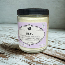Load image into Gallery viewer, Jar of lilac scented body butter with a purple label on a wooden surface. Whipped tallow lilac lotion in an 8oz glass jar with a rich, creamy texture, displayed on a rustic wooden surface. Natural, grass-fed tallow moisturizer for deep hydration, nourishing dry and sensitive skin. Handmade skincare product with a soft floral lilac scent, perfect for moisturizing, soothing, and restoring healthy skin.
